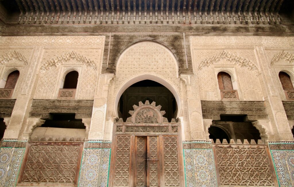 A carved wooden door leads to the interior courtyard of Bou Inania Madrasa