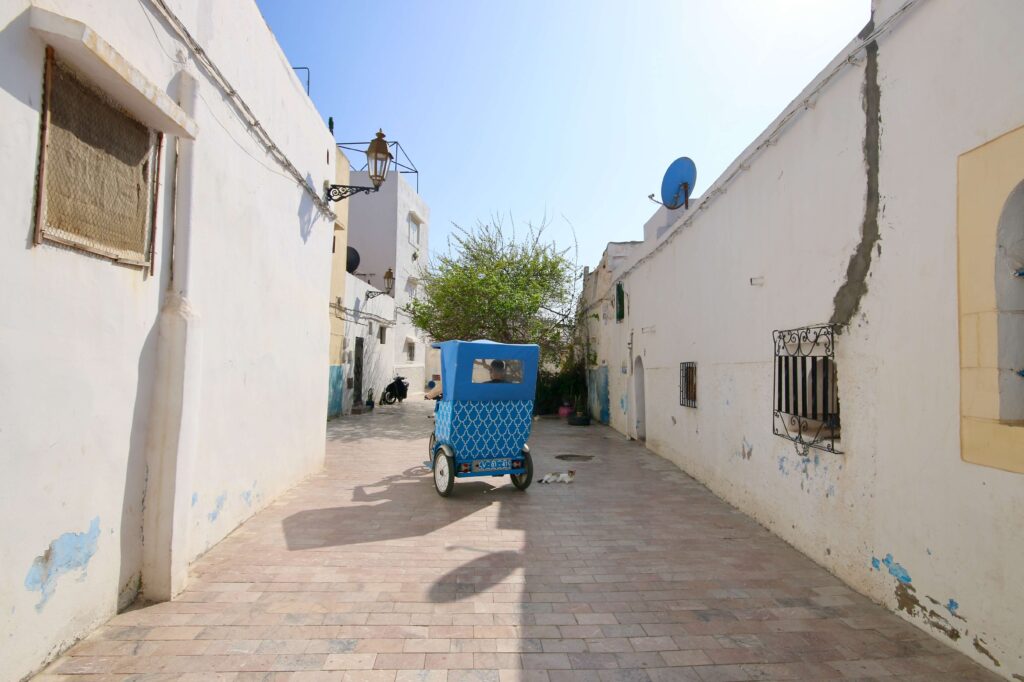 A blue tuk tuk driving through the whitewashed Kasbah of the Oudaias in Rabat