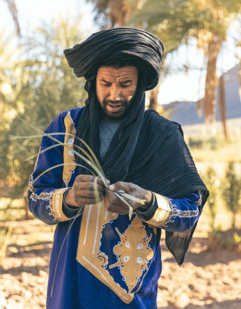 Travel guide to Taroudant: An Amazigh man weaving palm fronds in a Moroccan oasis