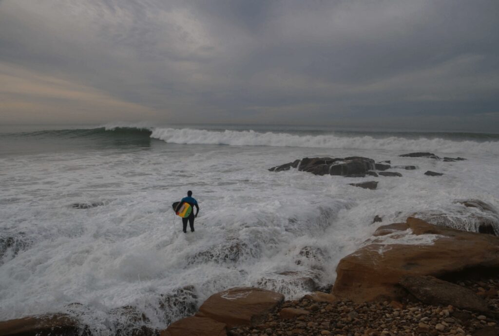 A surfer looks out toward Anchor Point on the edge of Taghazout village