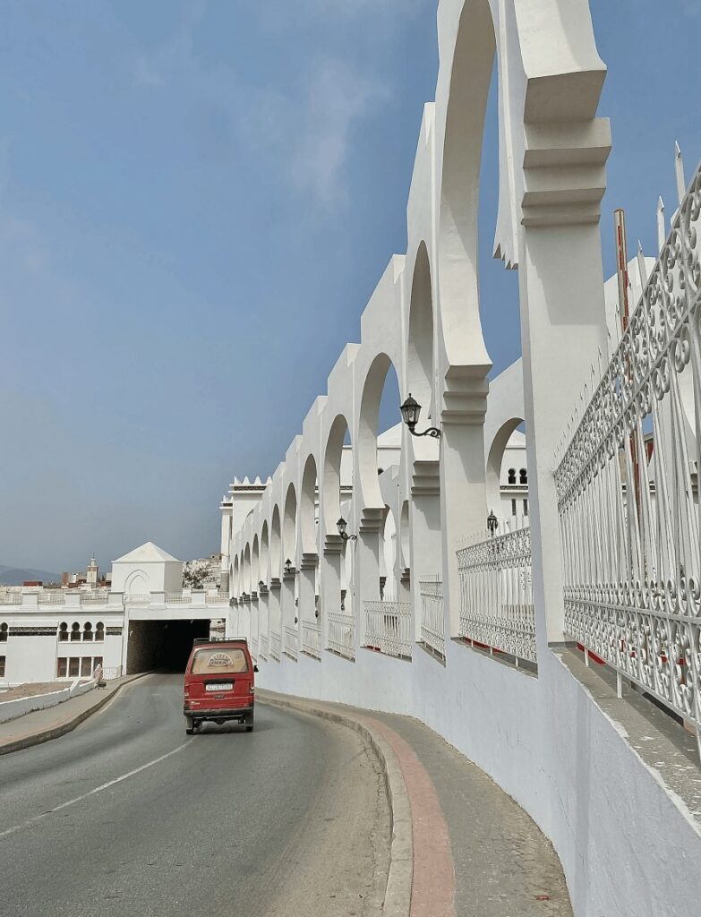 A red minivan drives along a street framed by arches in Tetouan