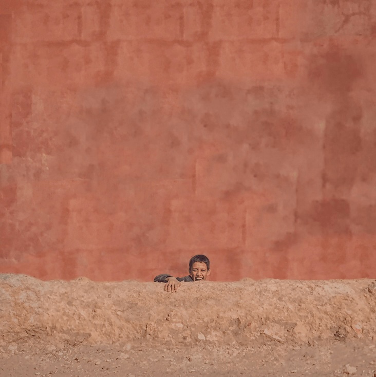 Travel guide to Taliouine: A Moroccan boy smiling in front of a ochre wall in Taliouine